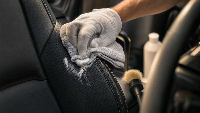 Entretien du cuir d'une voiture : application d'une mousse nettoyante au chiffon microfibre sur le flanc en cuir perforé d'un siège sport