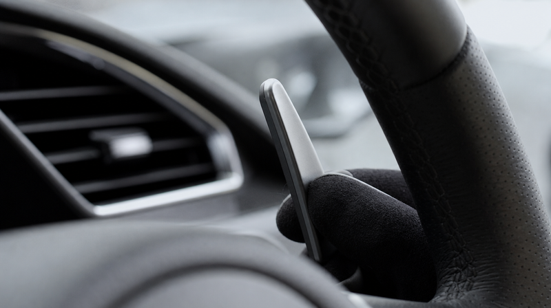 Palette au volant en aluminium anodisé tenue entre deux doigts, sur un coupé premium — Palette au volant voiture